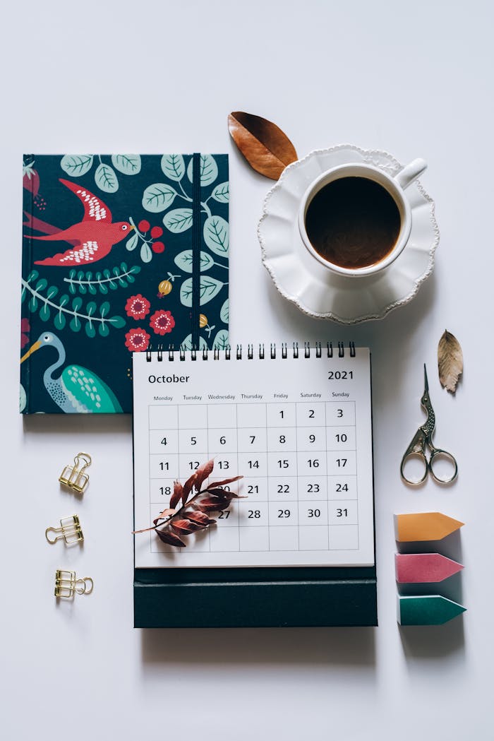 October-themed flat lay with calendar, coffee, notebook, and stationery on white background.